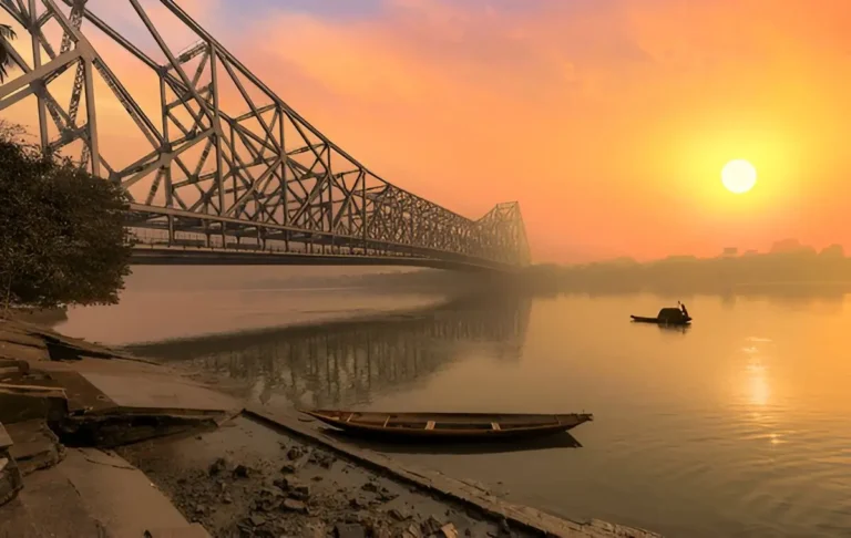 **Alt Text:**  
The serene Ganga River flowing through Kolkata, with iconic Howrah Bridge in the background, creating a picturesque and peaceful atmosphere.